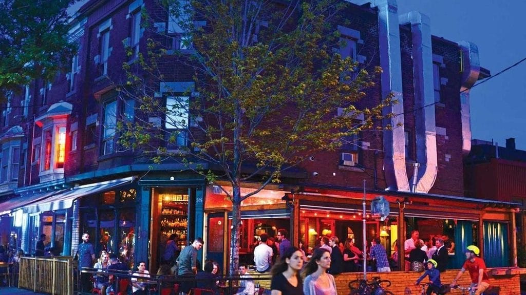 Guests gather outside Bar Raval at night on College Street in Toronto Spanish small plates and a standing-room social scene