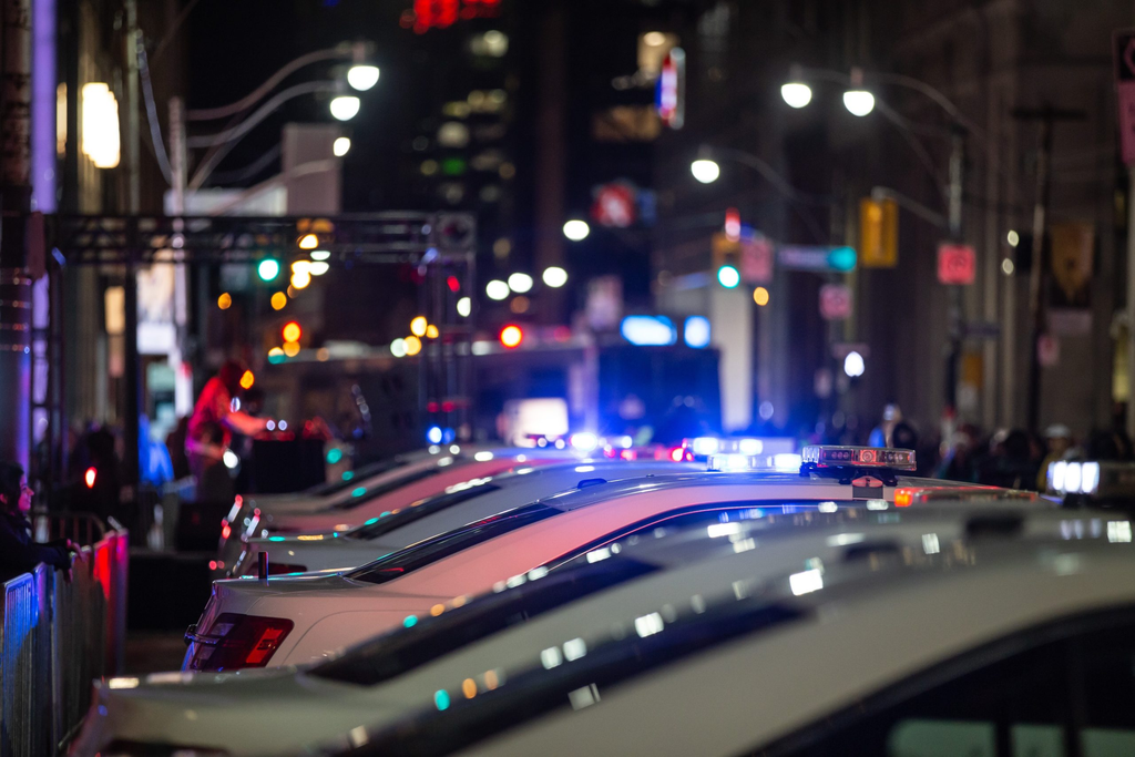 a line of police cars parked along a city street at night, with their emergency lights flashing blue and red.